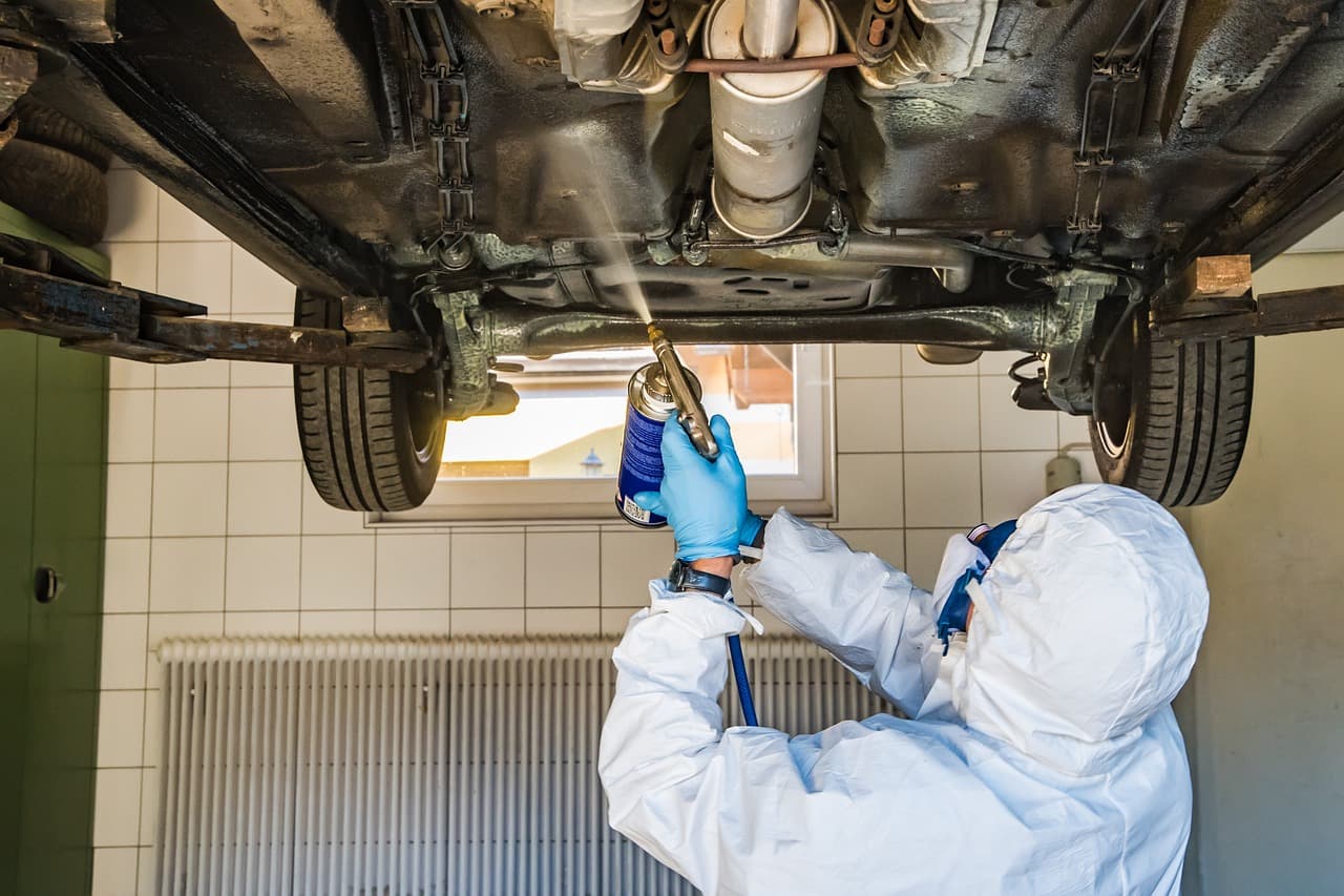 A technician in overalls working under a car raised on the ramp
